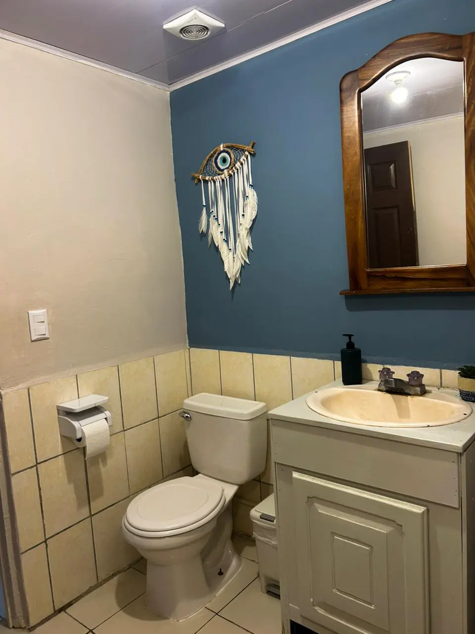 Hostel bathroom detail with dreamcatcher decoration and evil eye on blue wall.