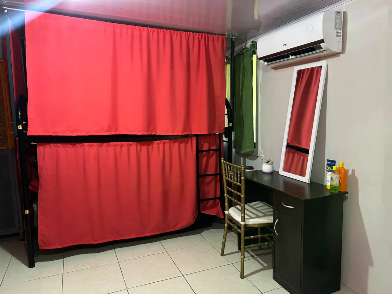 Female dorm with bunk bed, red privacy curtains, desk, and air conditioning.