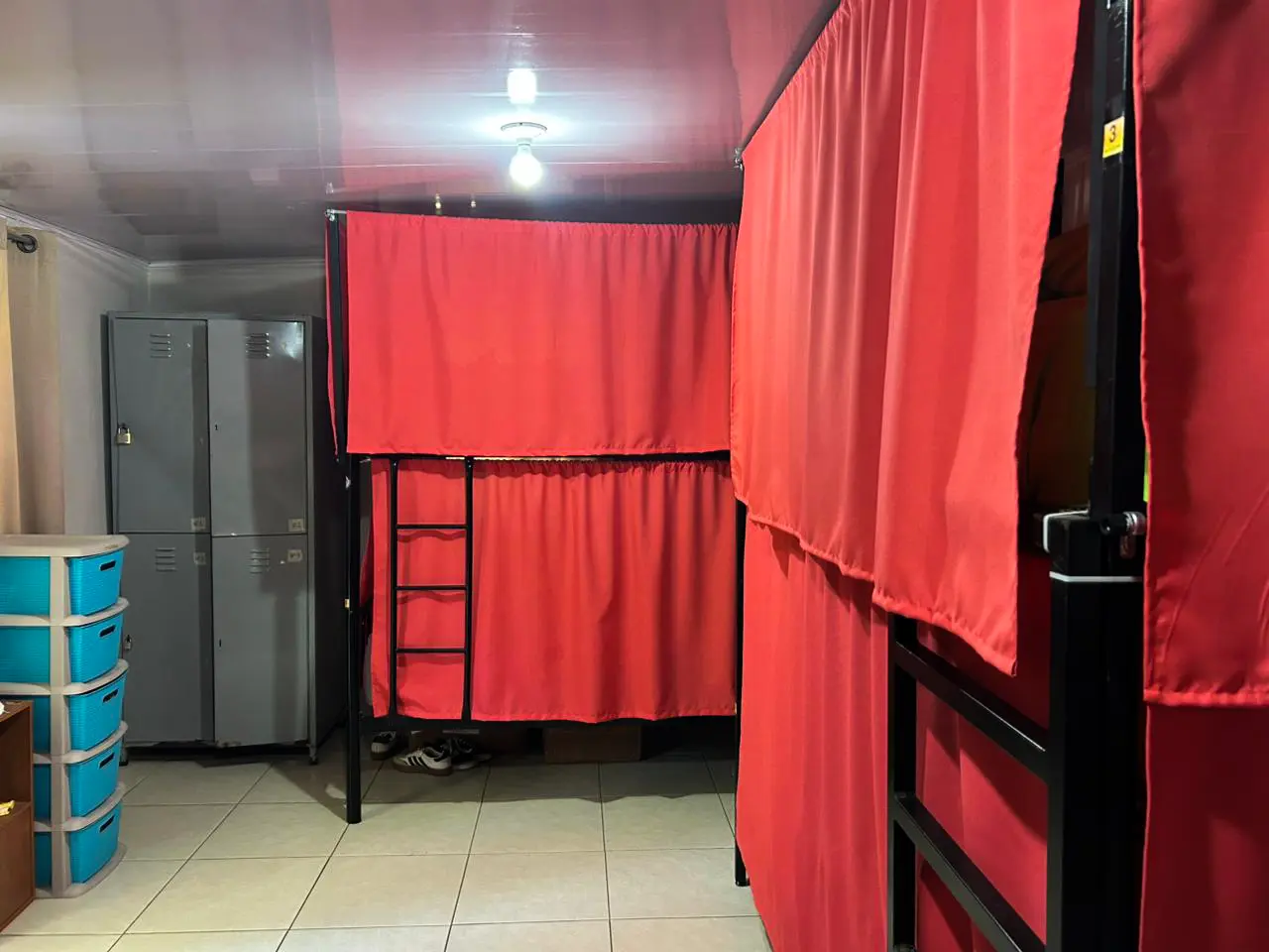Shared dormitory with curtained bunk beds and security lockers in the background.